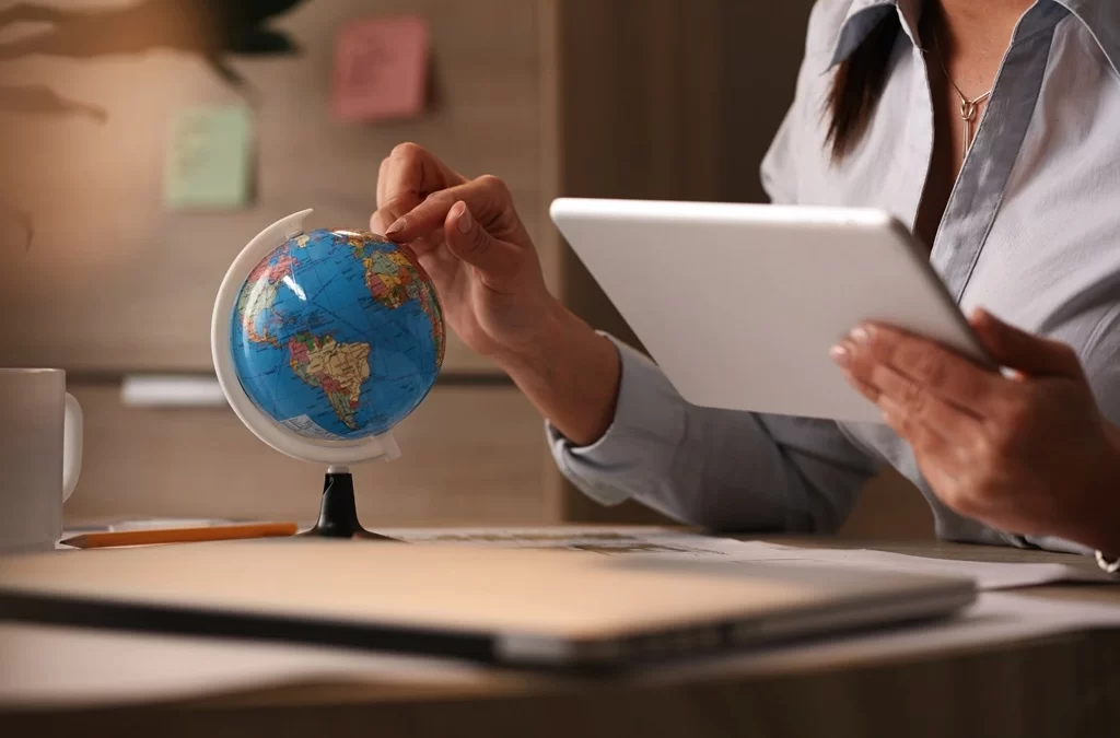 A person is using a tablet while pointing to a tiny global Earth.
